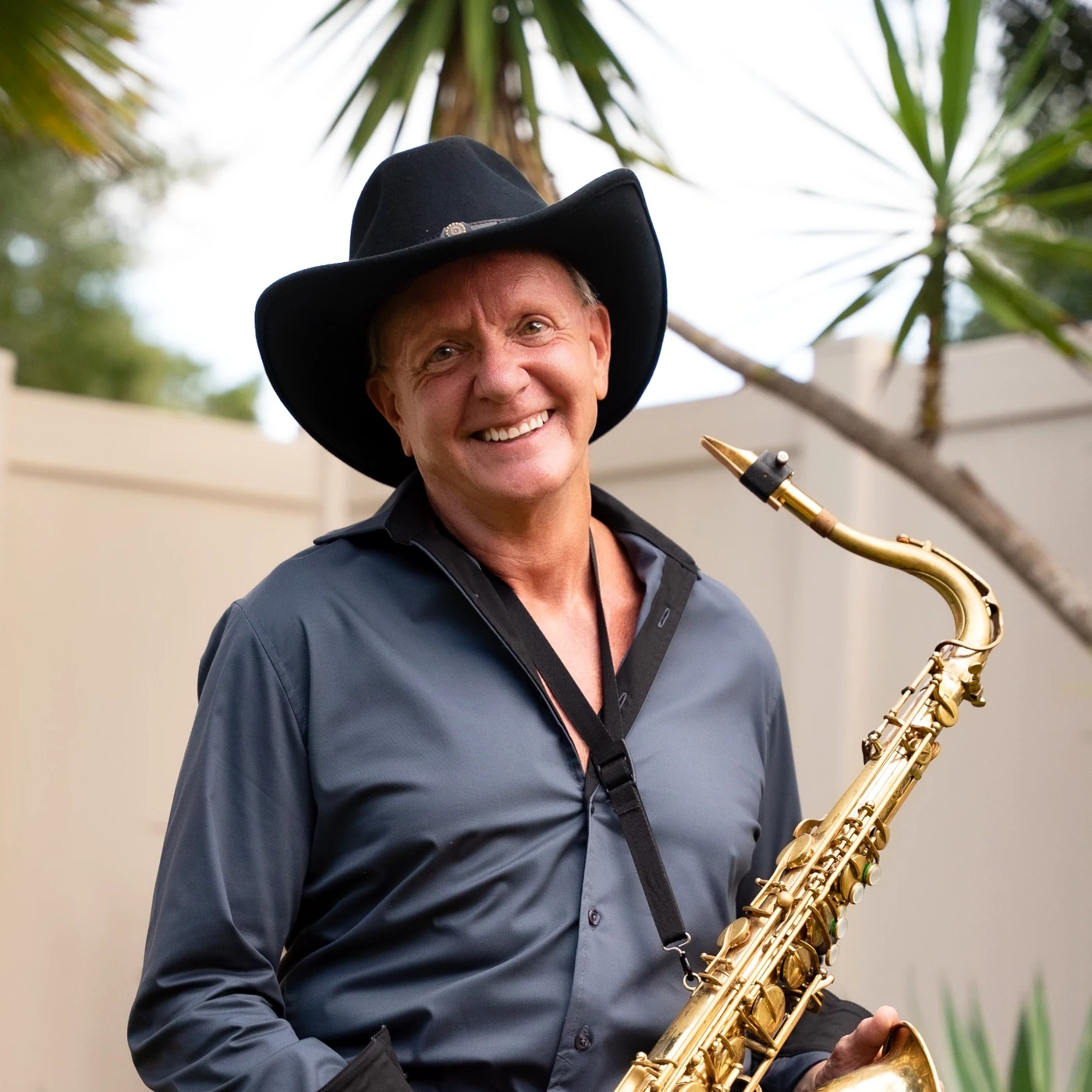 Portrait of David Maxx wearing a black cowboy hat with his saxophone